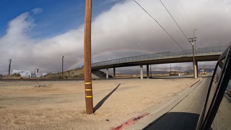 Un-Arco-Iris-Llena-El-Cielo-Después-De-Un-Raro-Chaparrón-En-El-Desierto-De-Mojave-Del-Sur-De-California---Vista-Desde-Un-Auto-Conduciendo-Por-La-Autopista