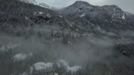 Ascending-aerial-shot-of-a-winter-mountain-covered-by-fog-and-frozen-trees,-Canada