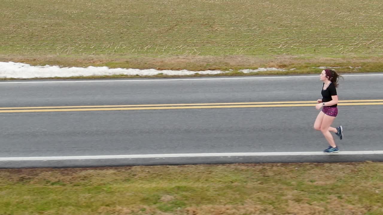 Good mental health theme preventing depression, anxiety, suicide. Young woman jogger enters frame, slow motion tracking shot features proper running form.