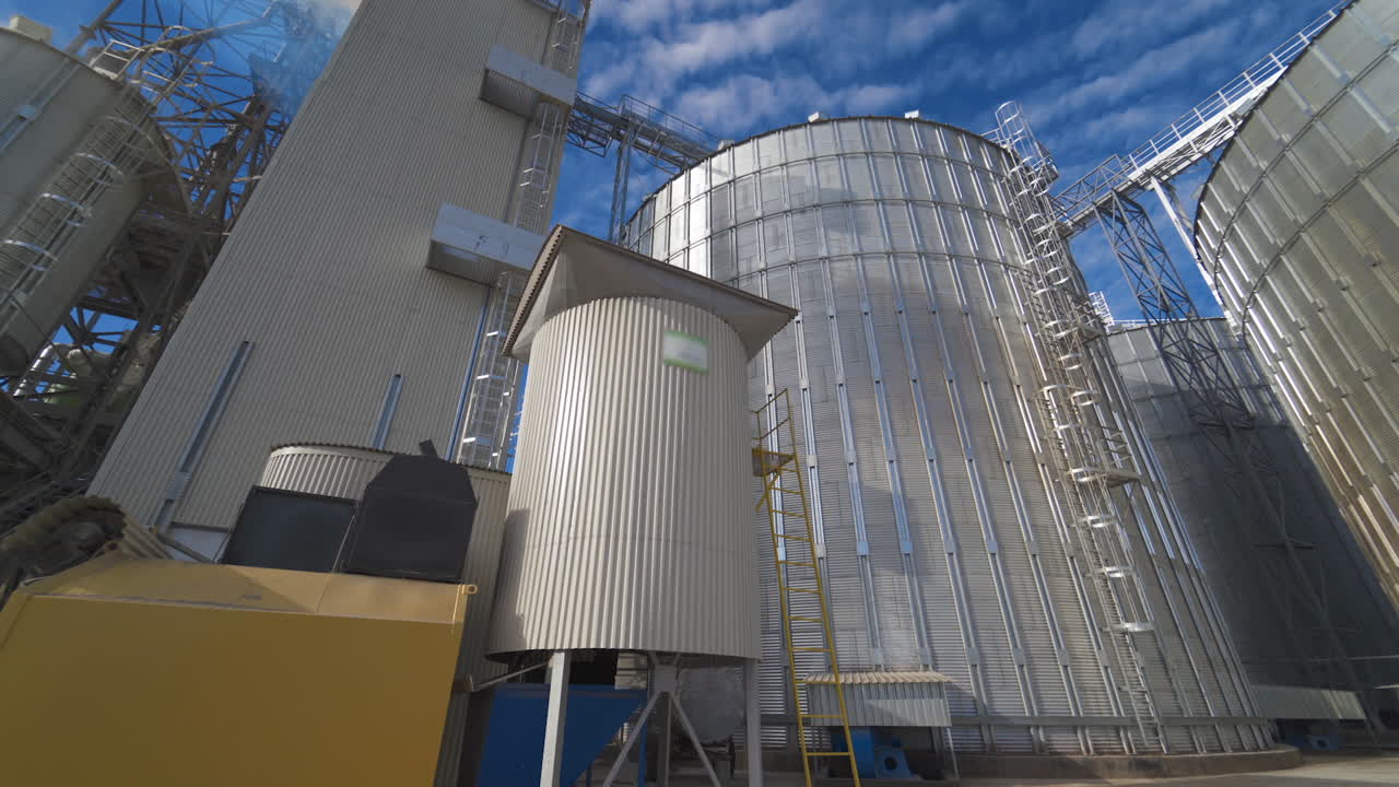 Large complex of agricultural factory. Industrial territory with large grain elevators in a sunny day. Modern silver grain elevators outdoors.