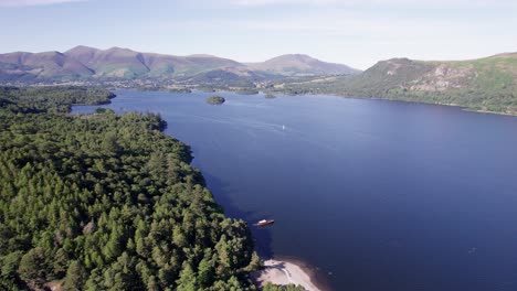 high drone shot flying right over derwent water with boats on the lake on a sunny day, lake district, cumbria, uk