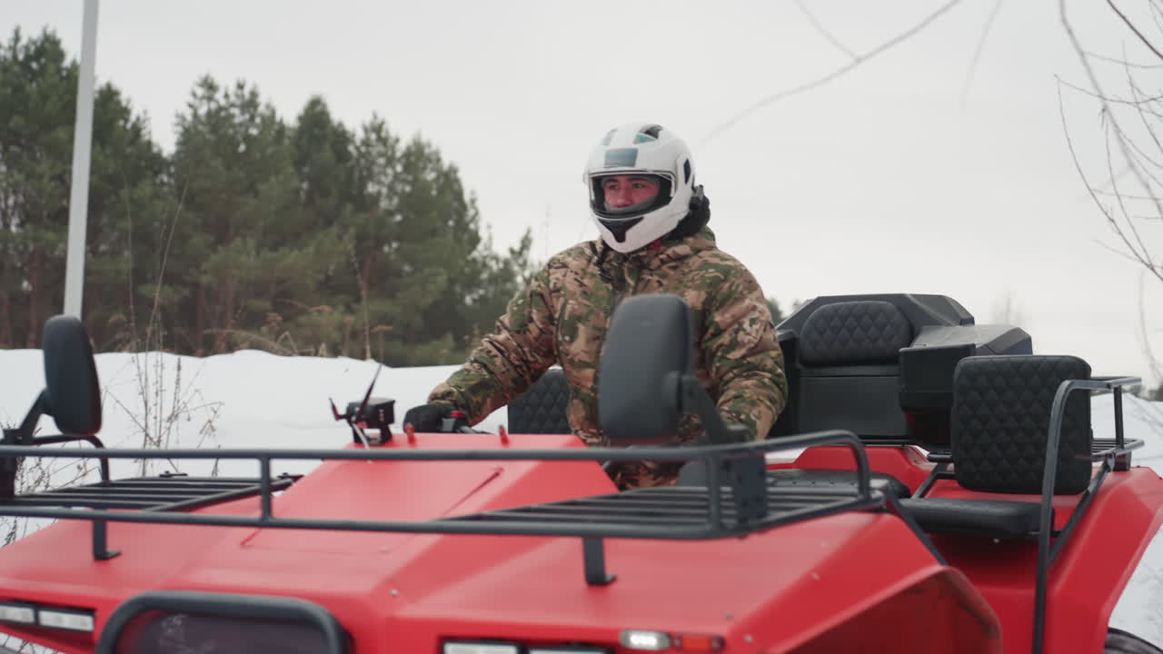 Pilota di quad rosso sfreccia nella neve, manovrando con maestria su un sentiero ghiacciato tra i pini. Il conducente, con casco e giacca mimetica, affronta solchi profondi. Primo piano degli pneumatici ghiacciati che sollevano neve. Cielo coperto.