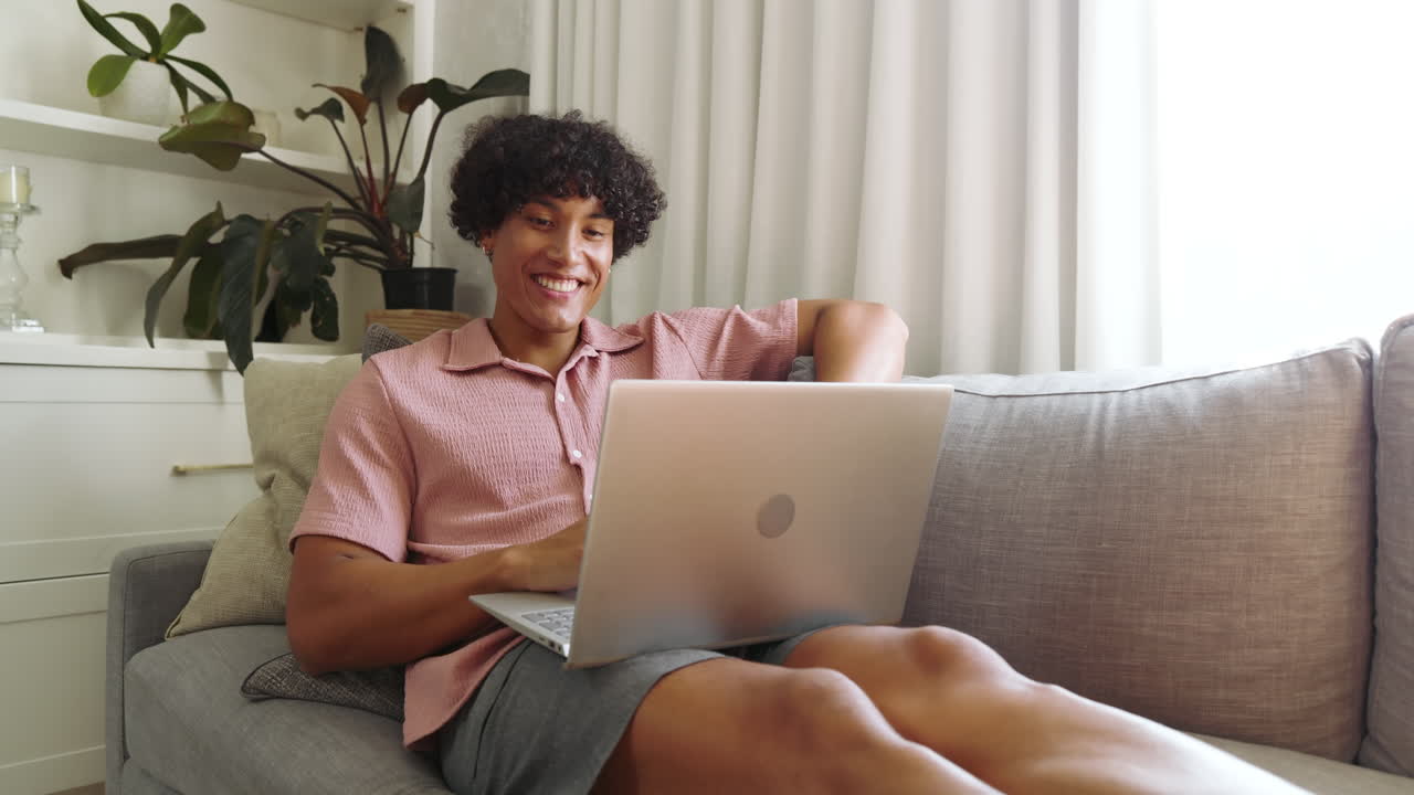 Relaxing on sofa, young man using laptop and gazing out window at home