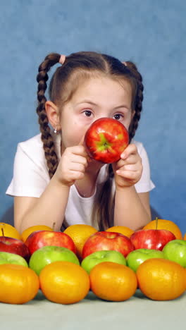 little girl sits at table. happy child girl and lot of fruit. vertical video
