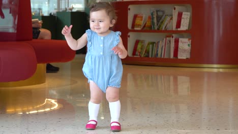 cute little baby girl standing alone in a book store and in hurry wobble to her mother with laughter