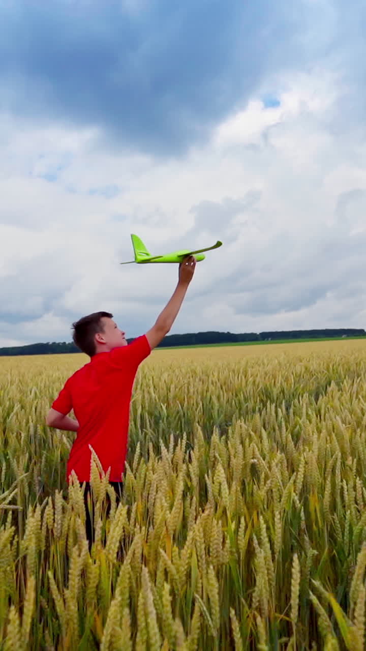Happy boy runs on field. Boy in a red t-shirt launches toy plane in agricultural land. Summer vacation outdoors. Slow motion. Vertical video