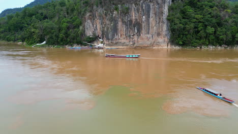 drone tracks laotian boat up the dirty mekong river past pak ou caves