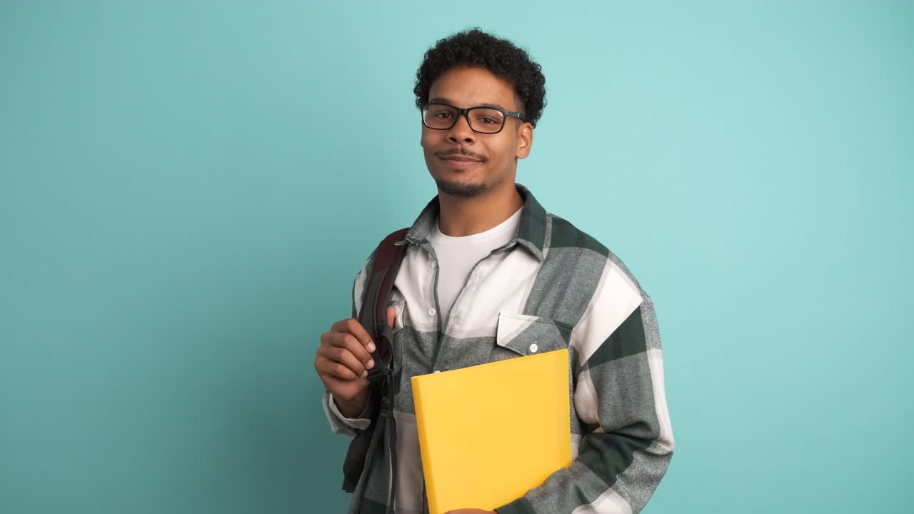 Happy male university student with backpack and books in blue studio