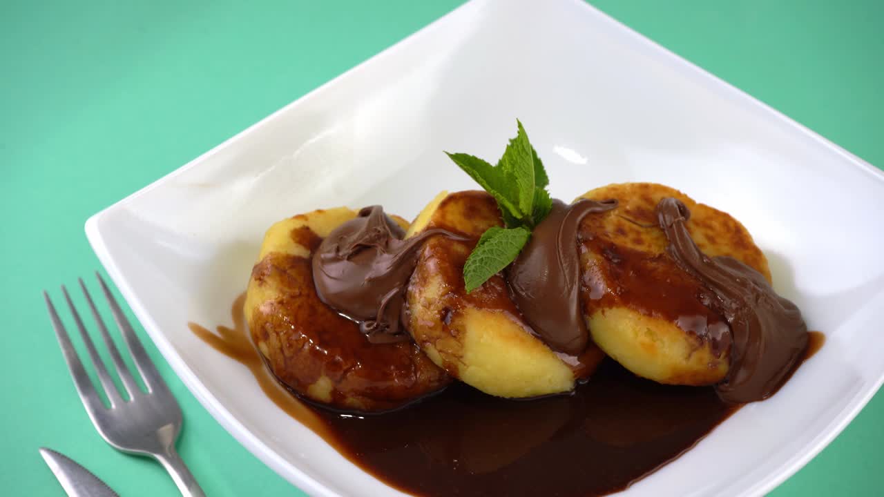 Portion of cheesecakes on a white plate with chocolate sauce and topping. Curd pancakes with mint. Baked food. Breakfast top view. Cheesecake