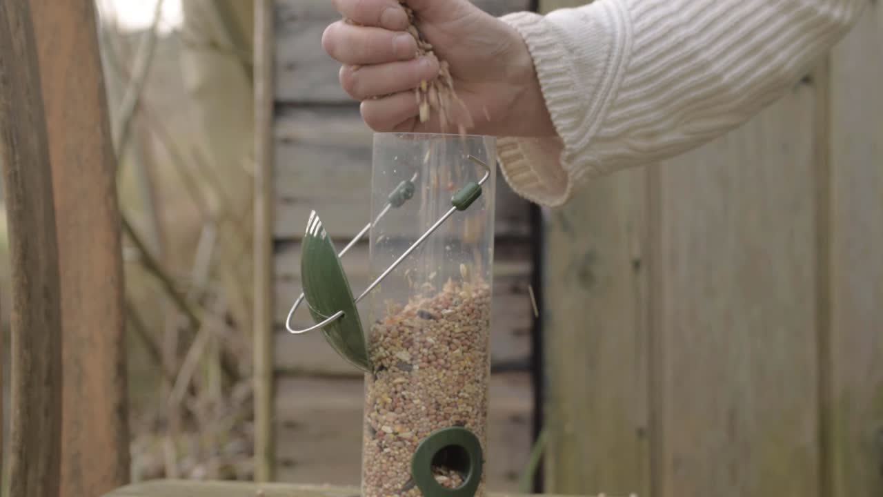 Hand filling a bird feeder with wild bird seed mix
