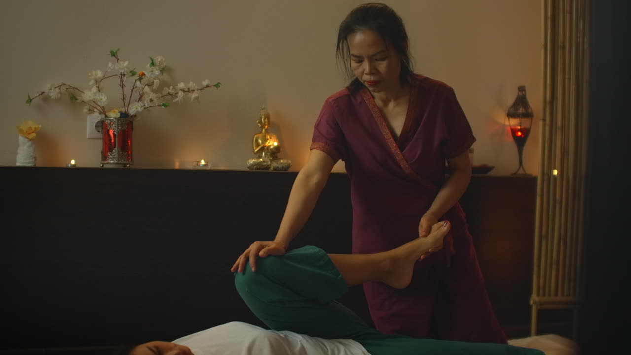 Asian performs massage in national clothes of Thailand. Asian Spa salon in Europe. Young Caucasian woman relaxes while performing massage.