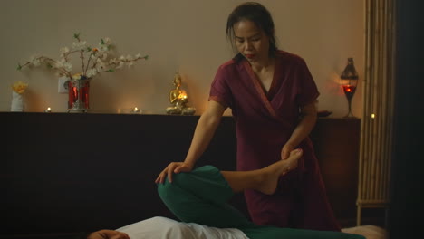 asiatique effectue un massage en vêtements nationaux de thaïlande. salon de spa asiatique en europe. jeune femme caucasienne se détend en effectuant un massage.