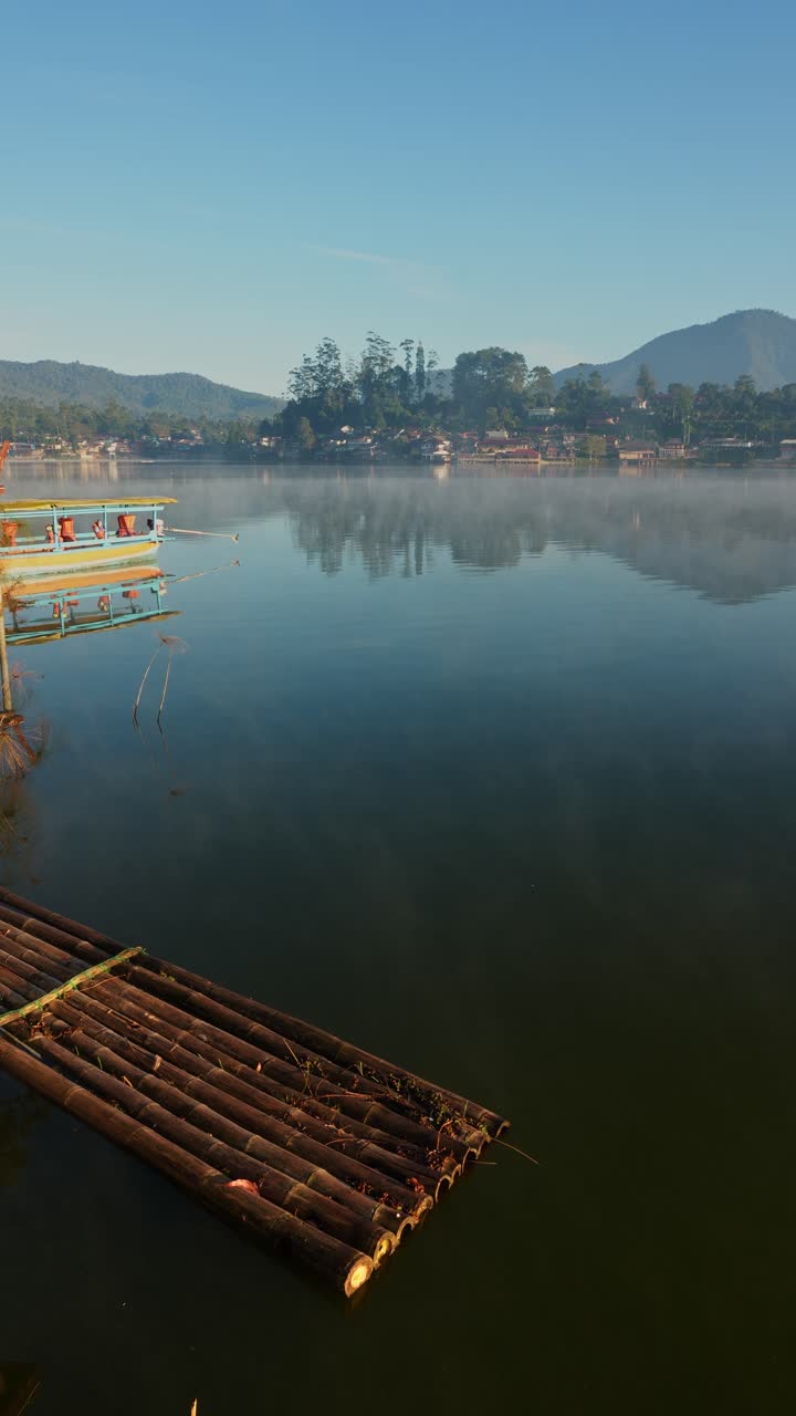 Serene Morning View Of Tranquil Lake With Mist Over The Water And Bamboo Raft In The Foreground