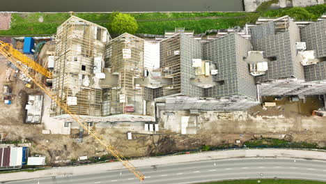 aerial view of a construction site with buildings under development, covered in scaffolding, and a crane extending across the site, surrounded by green areas