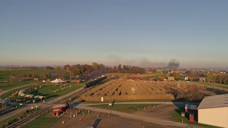 aerial view of an antique steam locomotive approaching pulling passenger cars and blowing smoke and steam during the golden hour in late afternoon