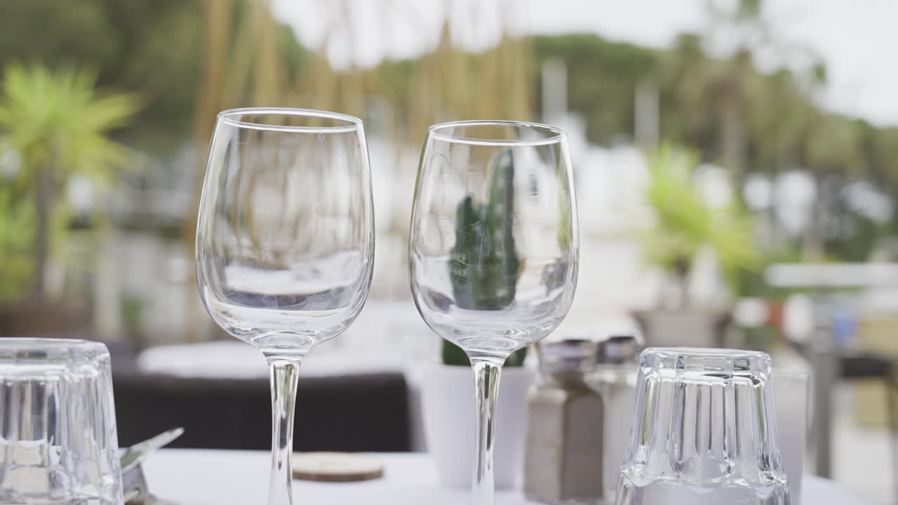 Primo piano di bicchieri su una tavola apparecchiata in una terrazza con persone che camminano sullo sfondo sfocato