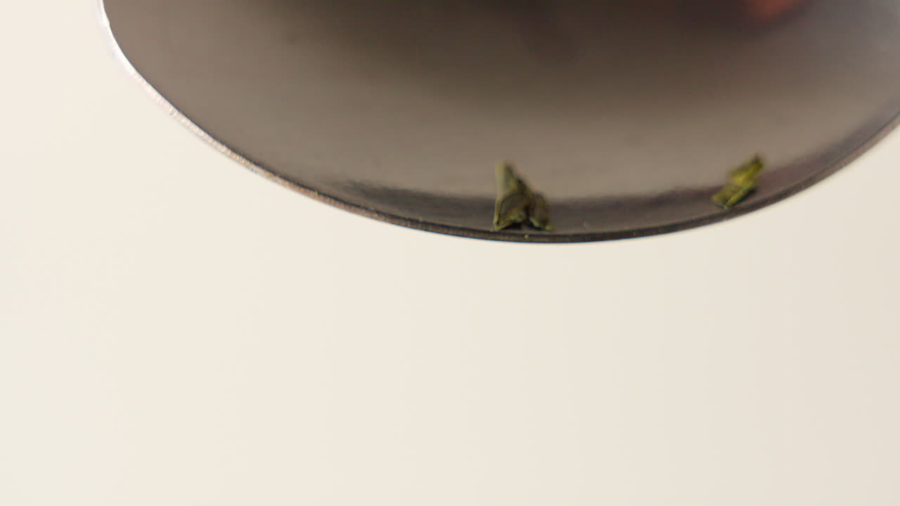 녹차 잎 더미가 100fps로 숟가락에서 떨어지고 있습니다.