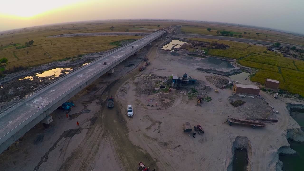 vista aérea del puente construido sobre el río con camiones pesados y maquinaria, granjas en el río