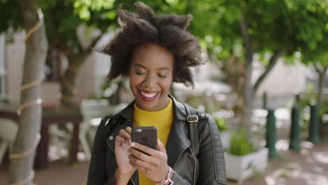 Retrato-De-Una-Estudiante-Afroamericana-De-Moda-Sonriendo-Disfrutando-De-Mensajes-De-Texto-Navegando-En-Línea-Usando-Un-Teléfono-Inteligente-Elegante-Mujer-Negra-En-La-Ciudad-Urbana