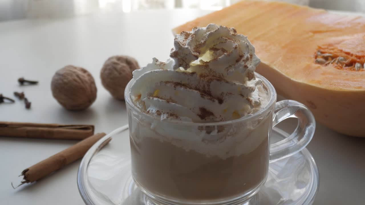 Zoom in on a clear glass cup with coffee or cocoa with cream, cinnamon, pumpkin, nuts and clove. Christmas flavors.