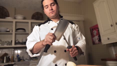 caucasian male chef sharpens stainless steel cleaver inside kitchen room, slow motion close up