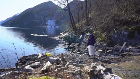 Woman-removing-plastic,-other-waste-from-Norway-fjord-shoreline
