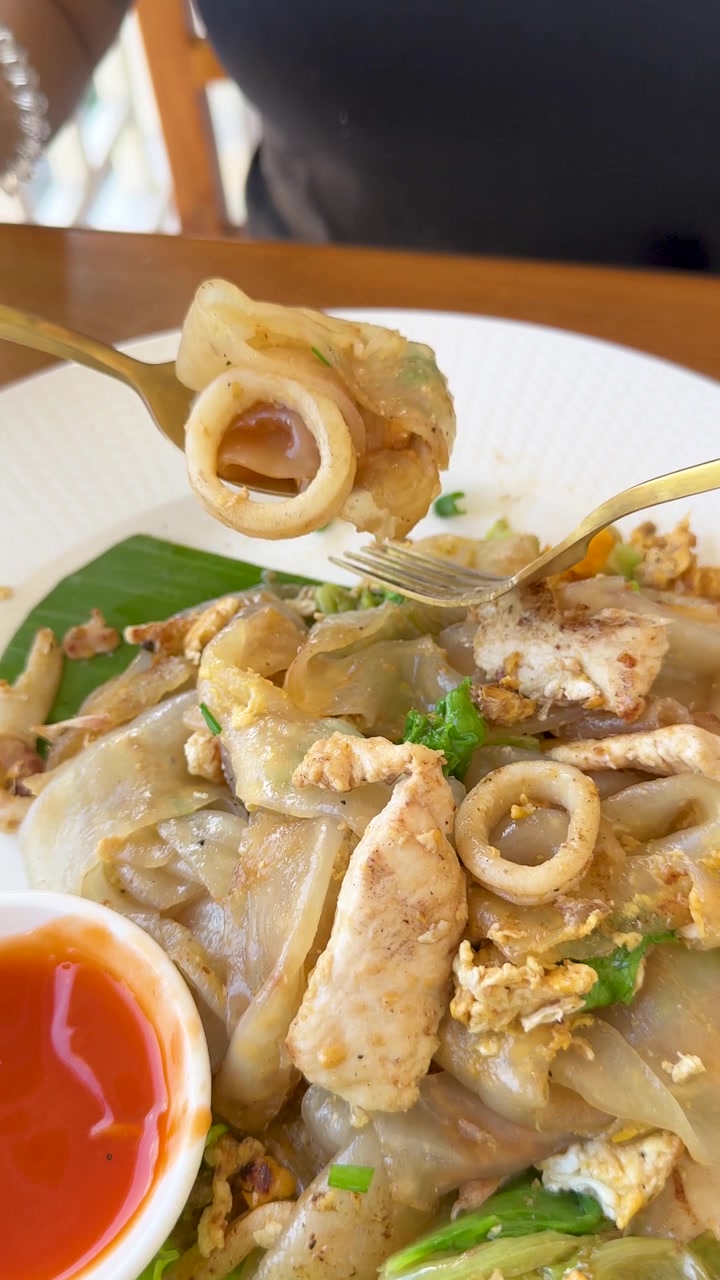 บุคคลใช้ส้อมคีบเส้นหมี่ผัดและปลาหมึกจากจานสีขาว