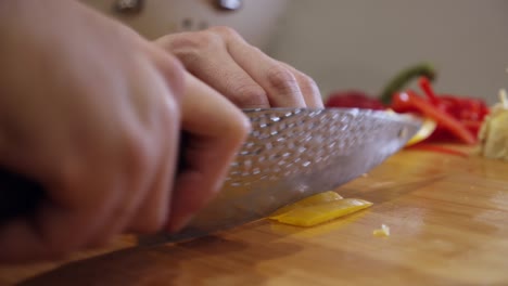 close up on steel knife slicing yellow color pepper on wooden cut board