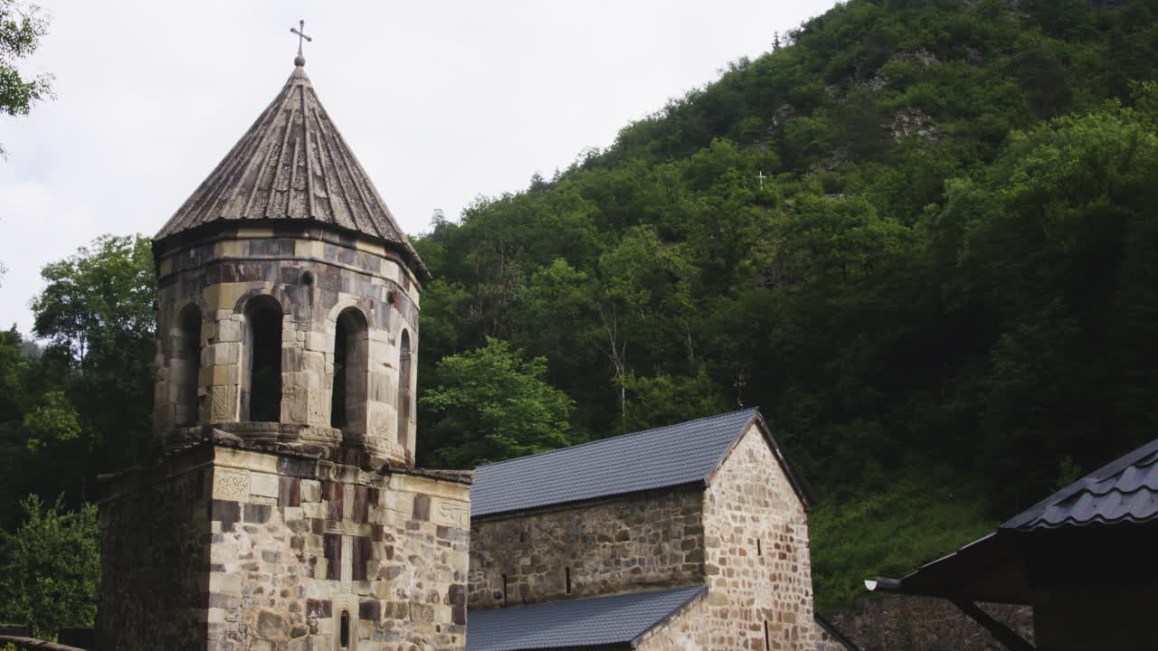 Bell tower and church of Mtsvane monastery below wooded hill, Georgia