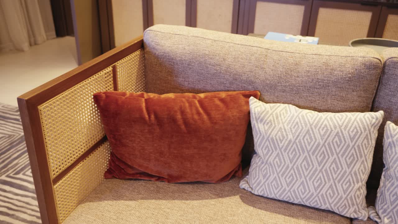 Detail shot focusing on the woven wicker textures of a designer armchair, transitioning to reveal a neutral-toned sofa with decorative pillows