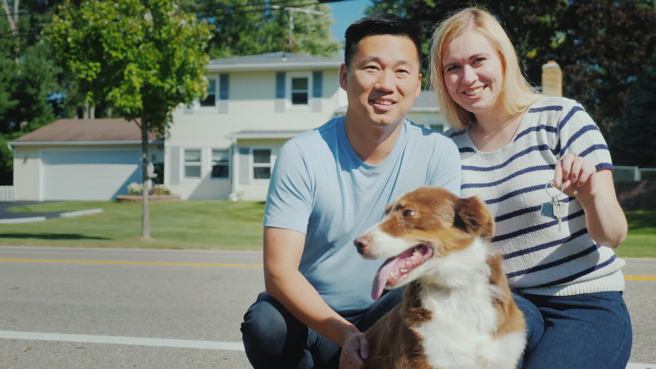 그들의 새 집 배경에 개가 있는 가족의 초상화 그들은 손에 열쇠를 쥐고 있다
