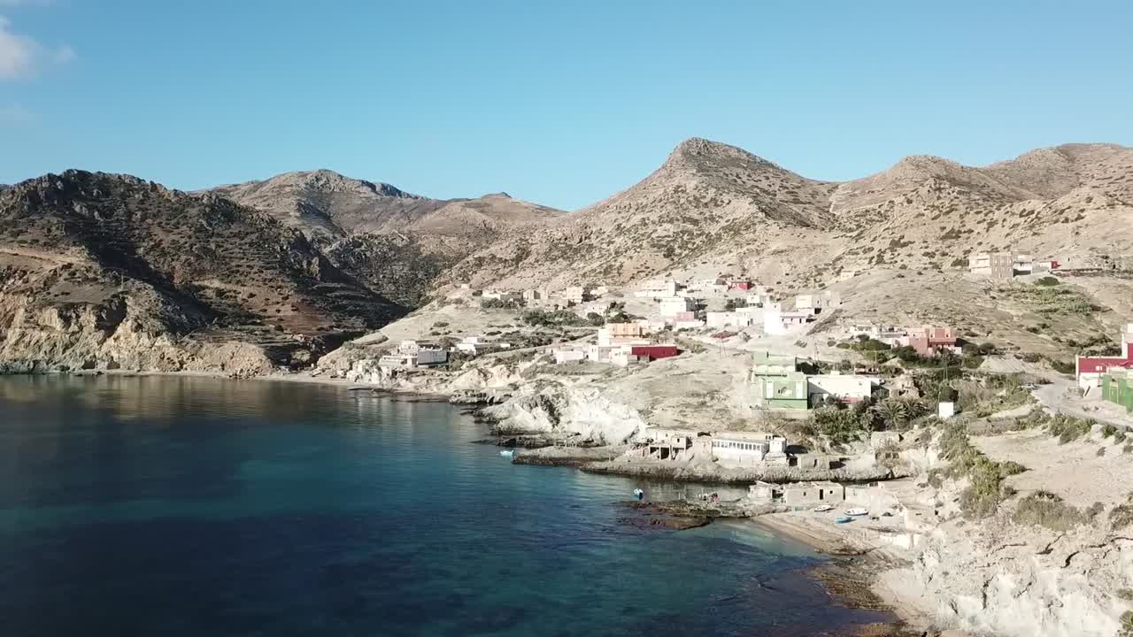 Cinematic drone shot tracking a flock of pink Greater Flamingos flying low over the blue waters of Nador's Mar Chica lagoon