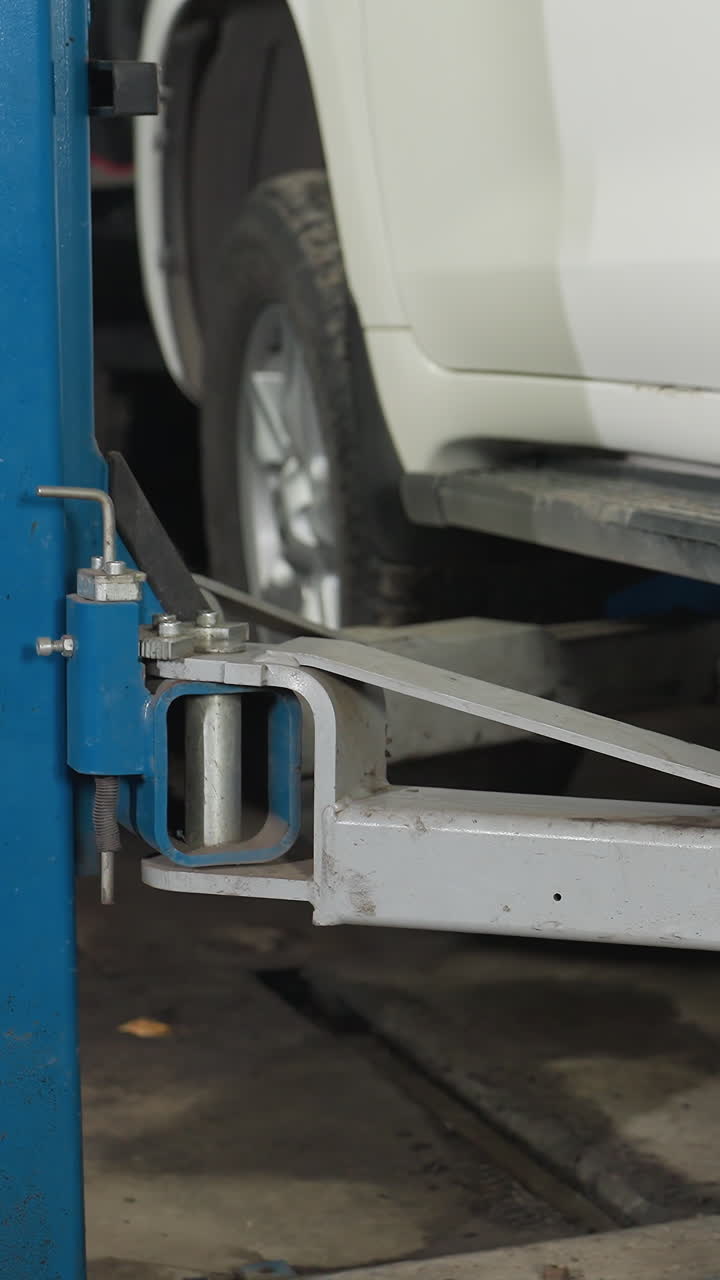 Detailed close-up of a white SUV being securely lowered from a hydraulic lift in an auto repair shop, focusing on the vehicle's side and lift mechanism