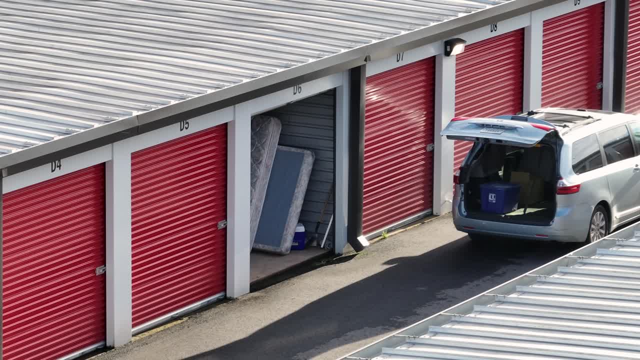 Vista aerea di un deposito self-service negli Stati Uniti, con box garage rossi avvolgibili e uno spazio di stoccaggio aperto con materassi all'interno. Auto carica presso un'unità a noleggio