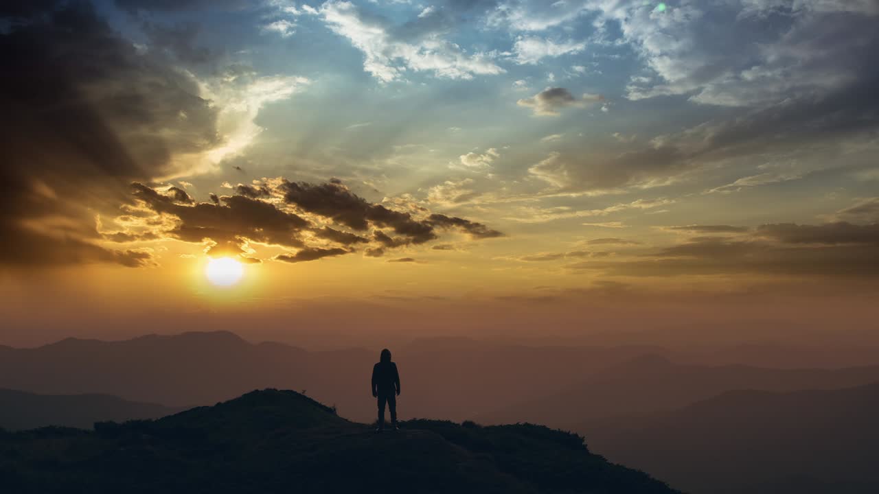 The man standing on a mountain top against a bright sunset. time lapse
