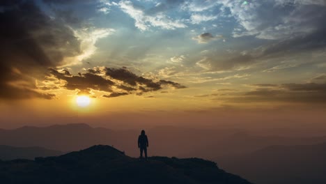 the man standing on a mountain top against a bright sunset. time lapse