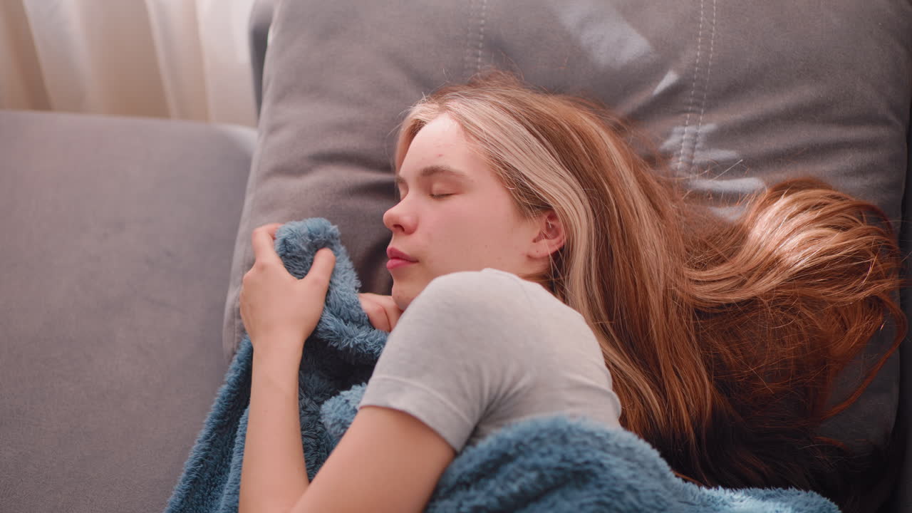 Top down view of dreamy lady holding blanket during sleep on couch with long hair spread out peacefully across pillow in gentle indoor lighting capturing moment of warmth