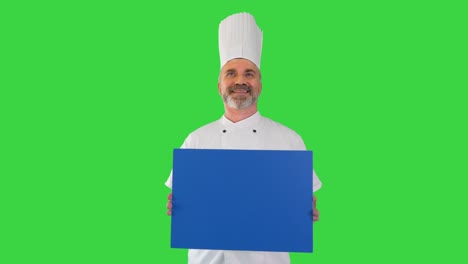 smiling male chef cook holding blank board on a green screen, chroma key