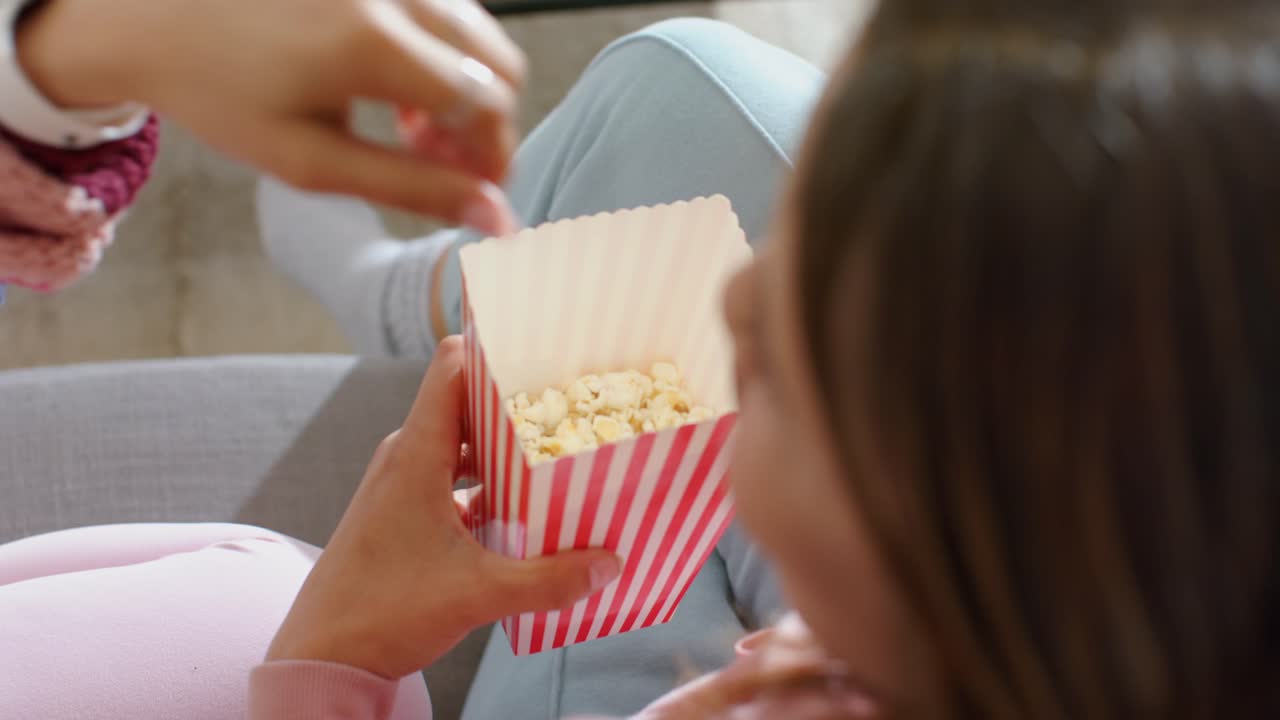 Strikker tar en pause fra strikkingen og tar popkorn fra en stripete popkornboks for å dele snacks på en grå sofa