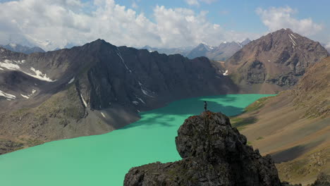 Revealing-drone-shot-of-a-man-standing-on-a-mountaintop-looking-at-the-Ala-Kol-lake-in-Kyrgyzstan