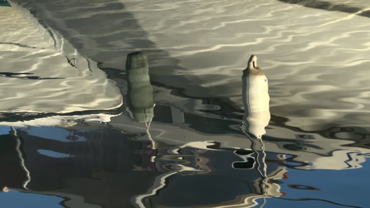 The reflection of the side of a boat docked in the water, with fenders hanging from its hull