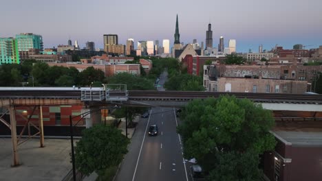 traffic driving under elevated train tracks in chicago with skyline view during sunset