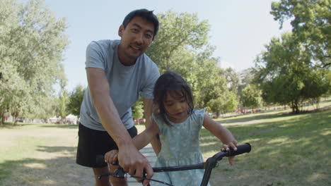 happy asian little girl learning to ride bicycle with her father at the park