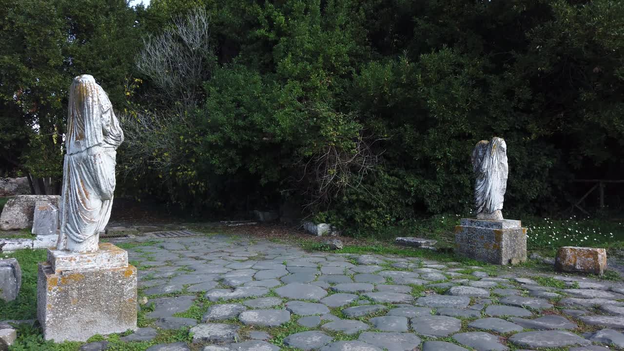 2 estatuas romanas a cada lado de una calzada romana en ostia antica, un sitio arqueológico mundialmente famoso de la antigua roma