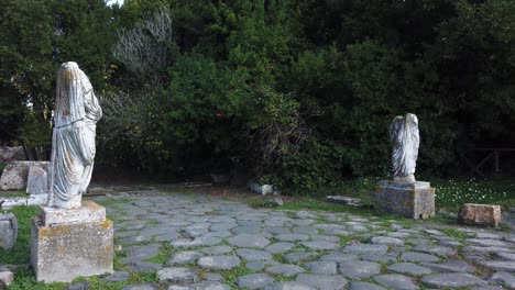 2 roman statues on each side of a roman road in ostia antica, a world famous archaeological site of ancient rome