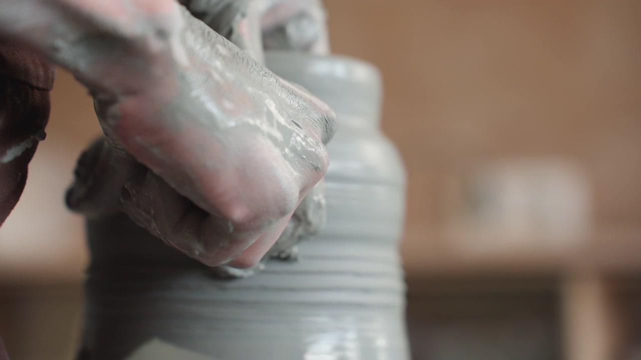 Closeup caucasian hands refining clay lip on spinning wheel in pottery studio, thumb smoothing rim of jar, steady rotation, warm workshop shelves in soft focus, patient craft practice