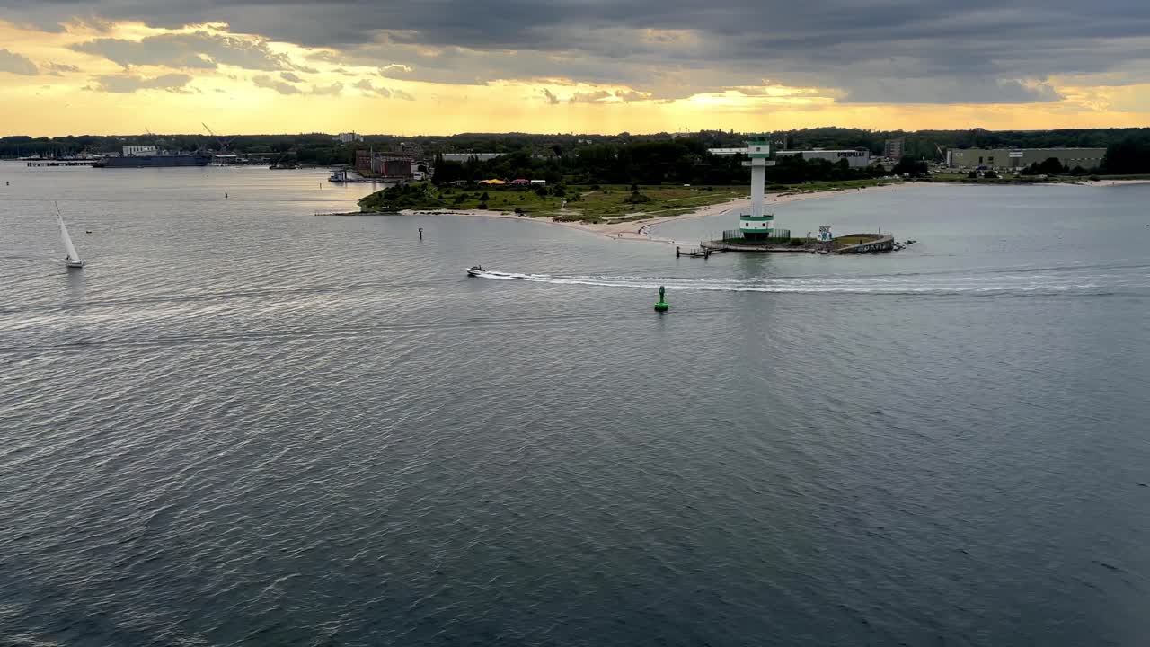 Sunset view of the Copenhagen coastline from a departing ship, featuring a sailboat, electric boat, modern lighthouse, and scenic harbor