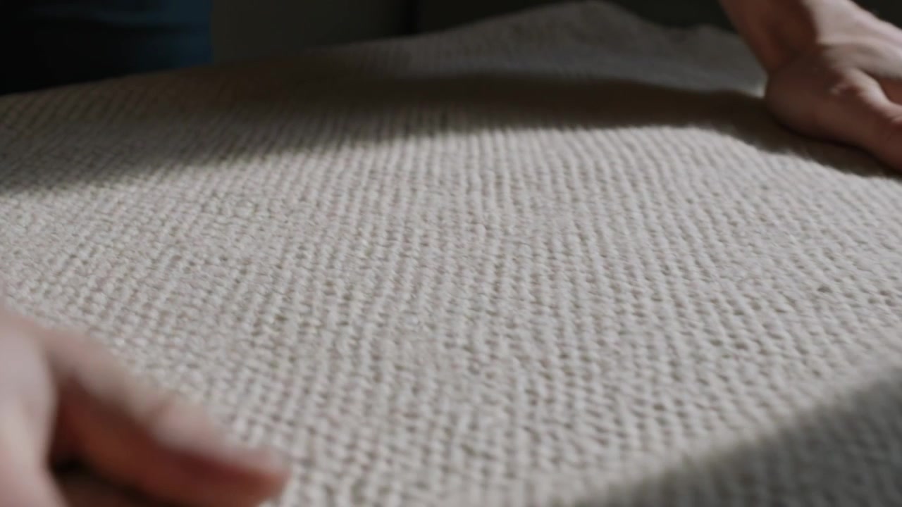 Avvicinandosi da destra, mani che premono, levigano e controllano una coperta tessuta sul divano, in maniche corte.