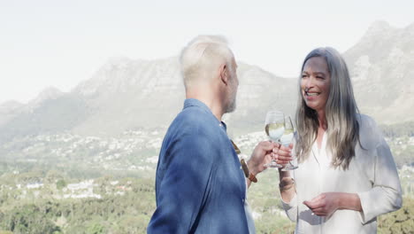 Feliz-Pareja-Caucásica-De-Mediana-Edad-Bebiendo-Vino-En-La-Terraza-De-Las-Montañas,-Cámara-Lenta