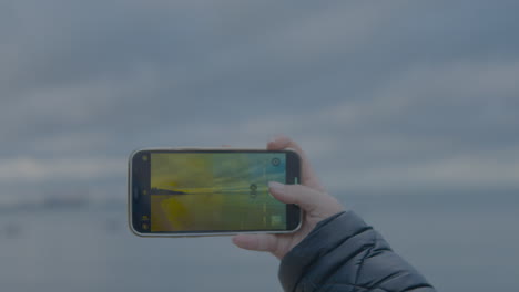 girl in black jacket take a photo of landscape by smartphone one hand